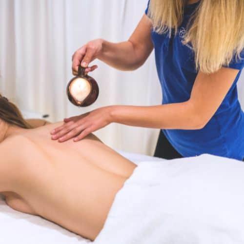 Terapeutka spa rozprowadza olejek ze świecy aromaterapeutycznej na plecach klientki