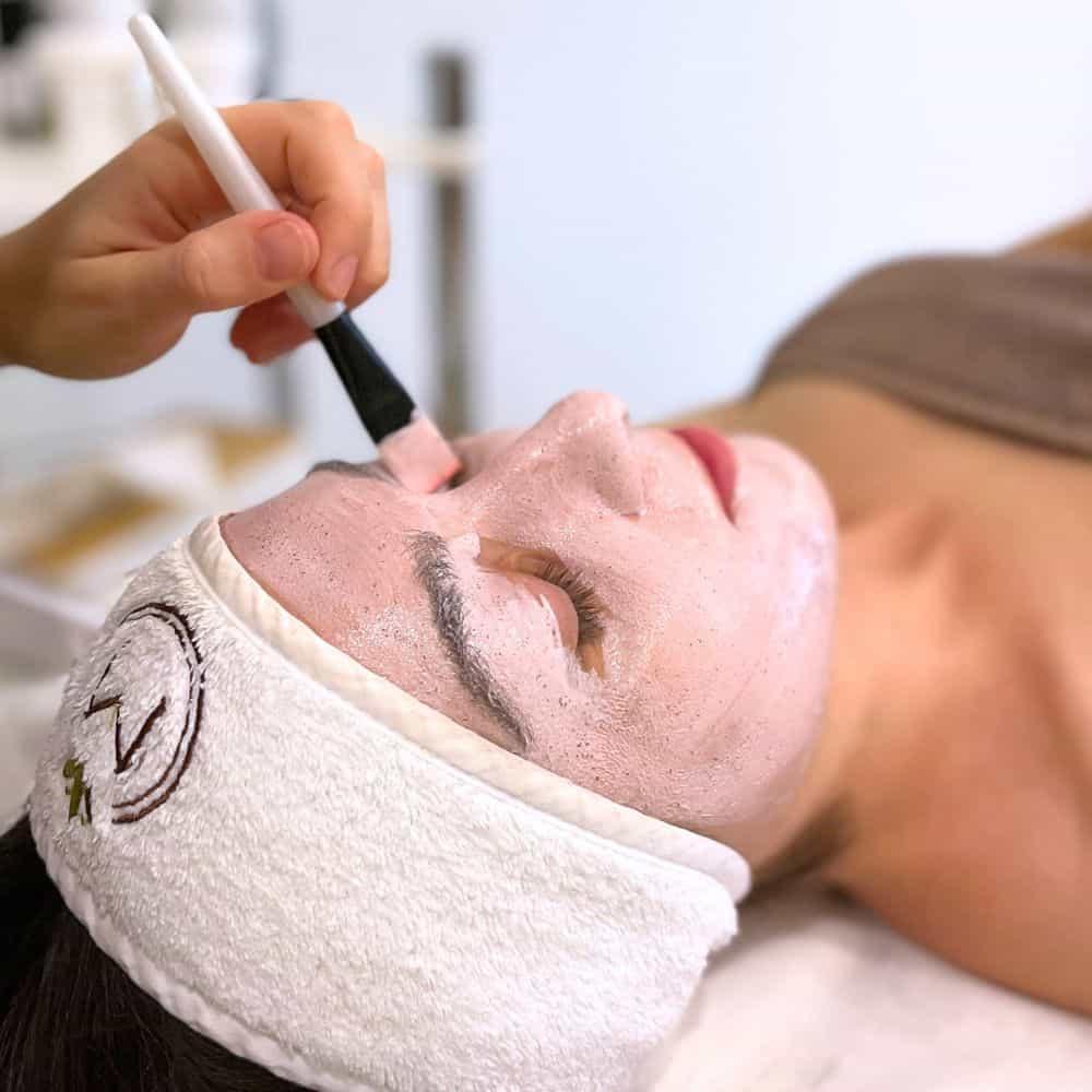 Kobieta relaksująca się podczas nakładania przez terapeutkę spa pędzelkiem peelingu na twarz