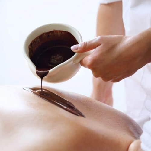 Terapeutka spa wylewająca ciepłą czekoladę na plecy klientki