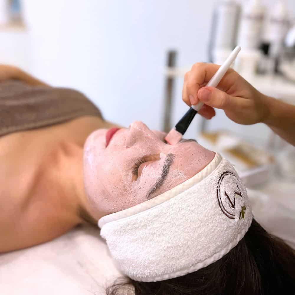 Kobieta relaksująca się podczas nakładania przez terapeutkę spa pędzelkiem peelingu na twarz