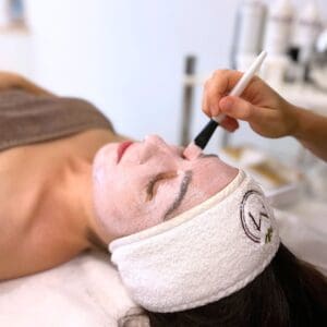 Kobieta relaksująca się podczas nakładania przez terapeutkę spa pędzelkiem peelingu na twarz